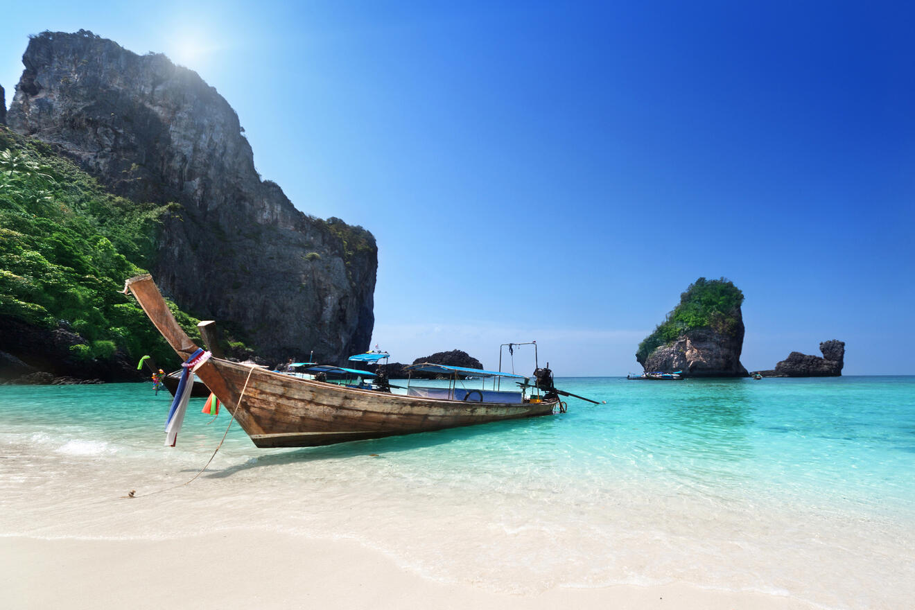 A traditional wooden boat on a serene beach with turquoise water and towering cliffs.